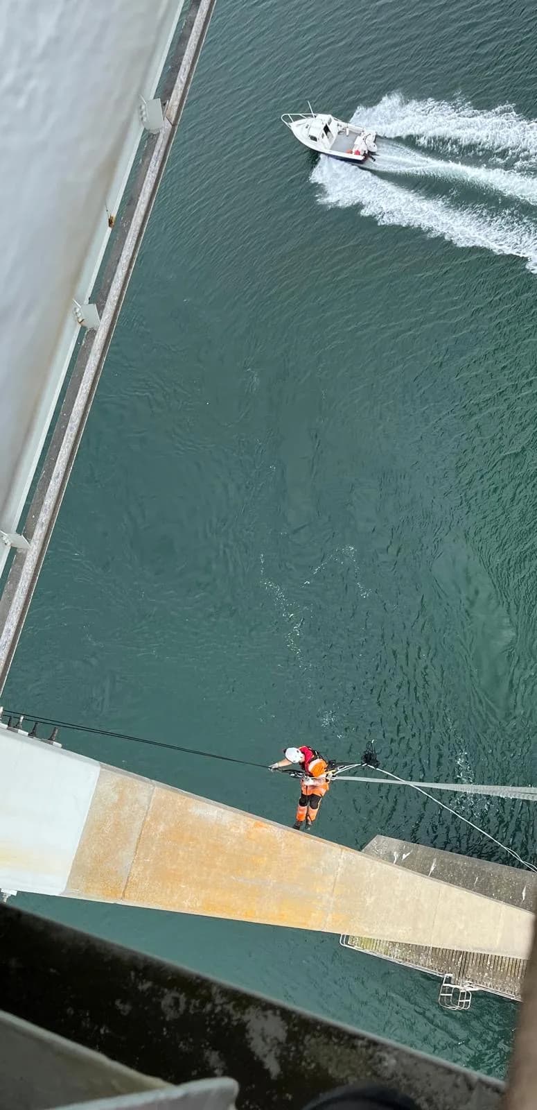 Technician working on a pier head high above the water as a boat passes below
