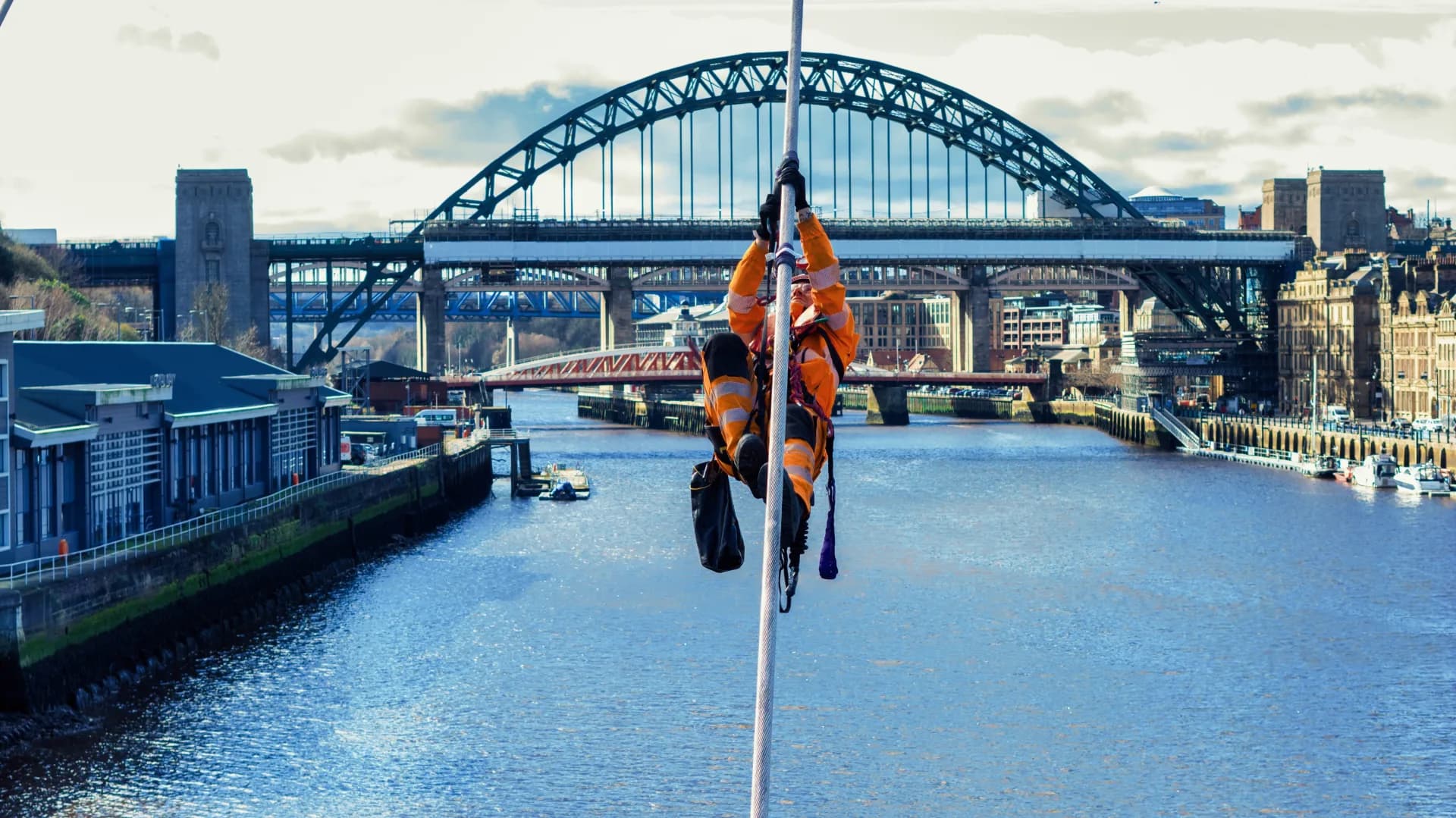 Technician climbing a bridge cable above the River Tyne, with the Tyne Bridge behind