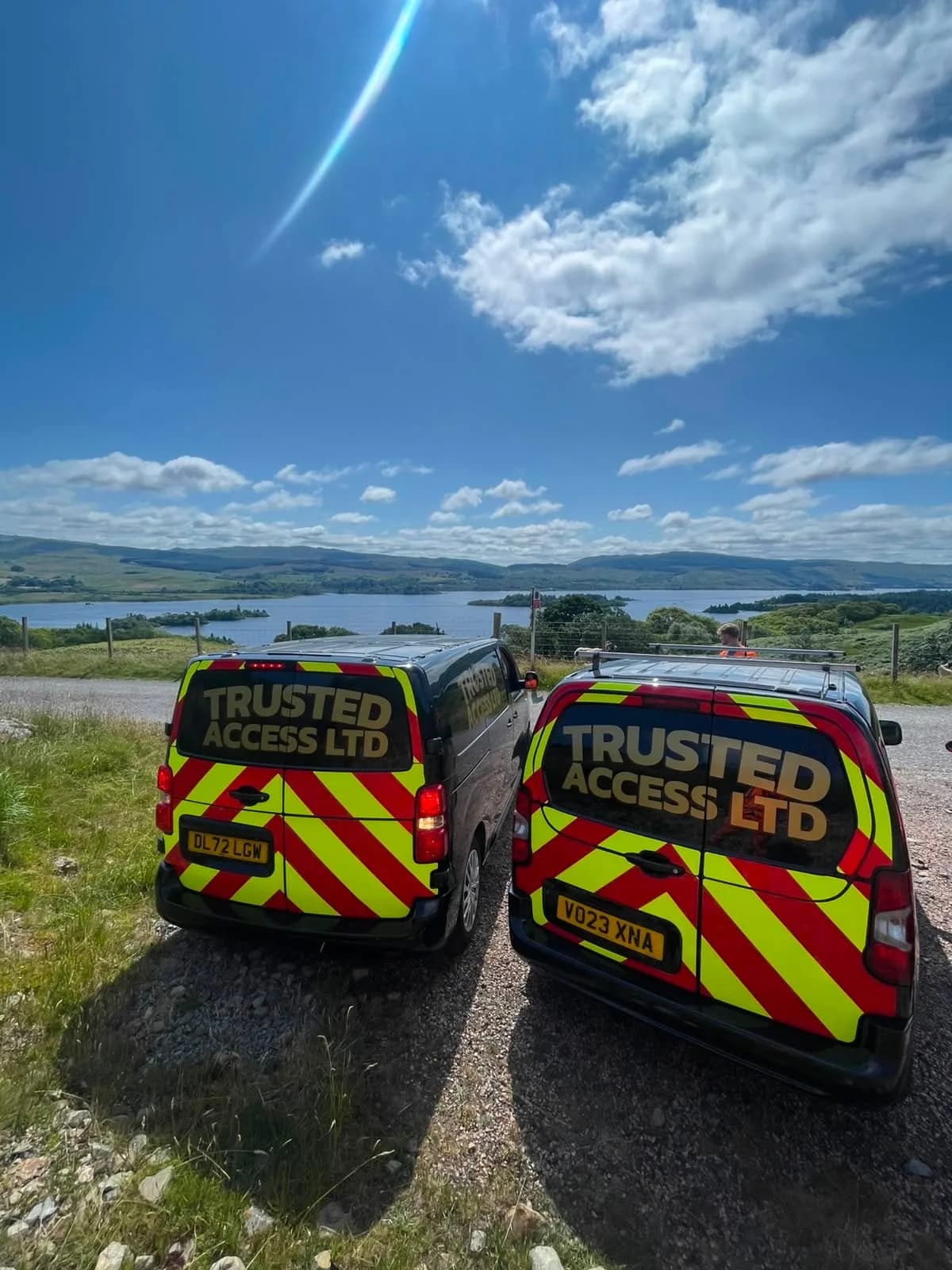 Two liveried Trusted Access vans parked above a loch